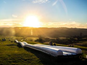extremely long waterslide, sunset, greenery, very large field, mountains