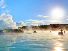 several people relax in the blue lagoon hot spring during the day with mountains in background
