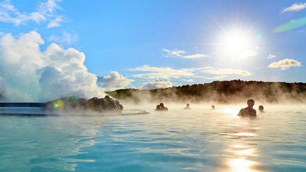 several people relax in the blue lagoon hot spring during the day with mountains in background