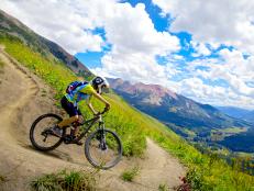 young boy rides mountain bike down trail with mountains in background on sunny day