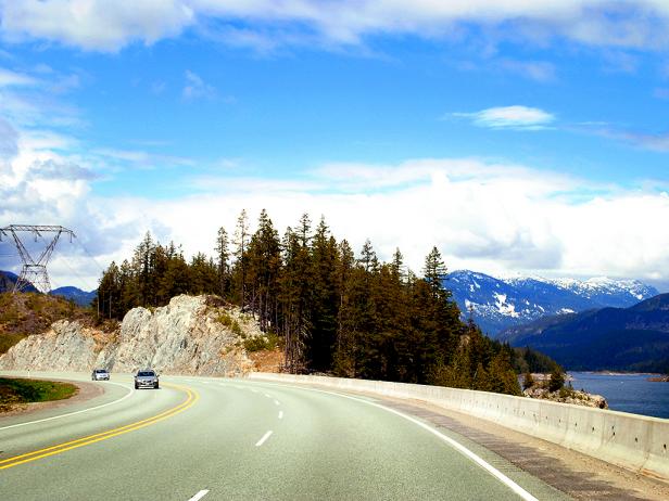 curved highway next to lake with trees and mountain in distance curved highway next to lake with trees and mountain in distance