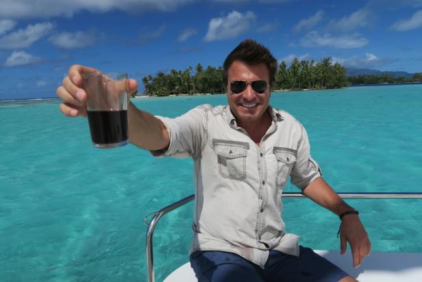 Host Jack Maxwell holds up a glass to toas the camera while sailing around Tahiti.