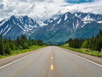 Smooth Alaskan highway leading towards mountains in summer
