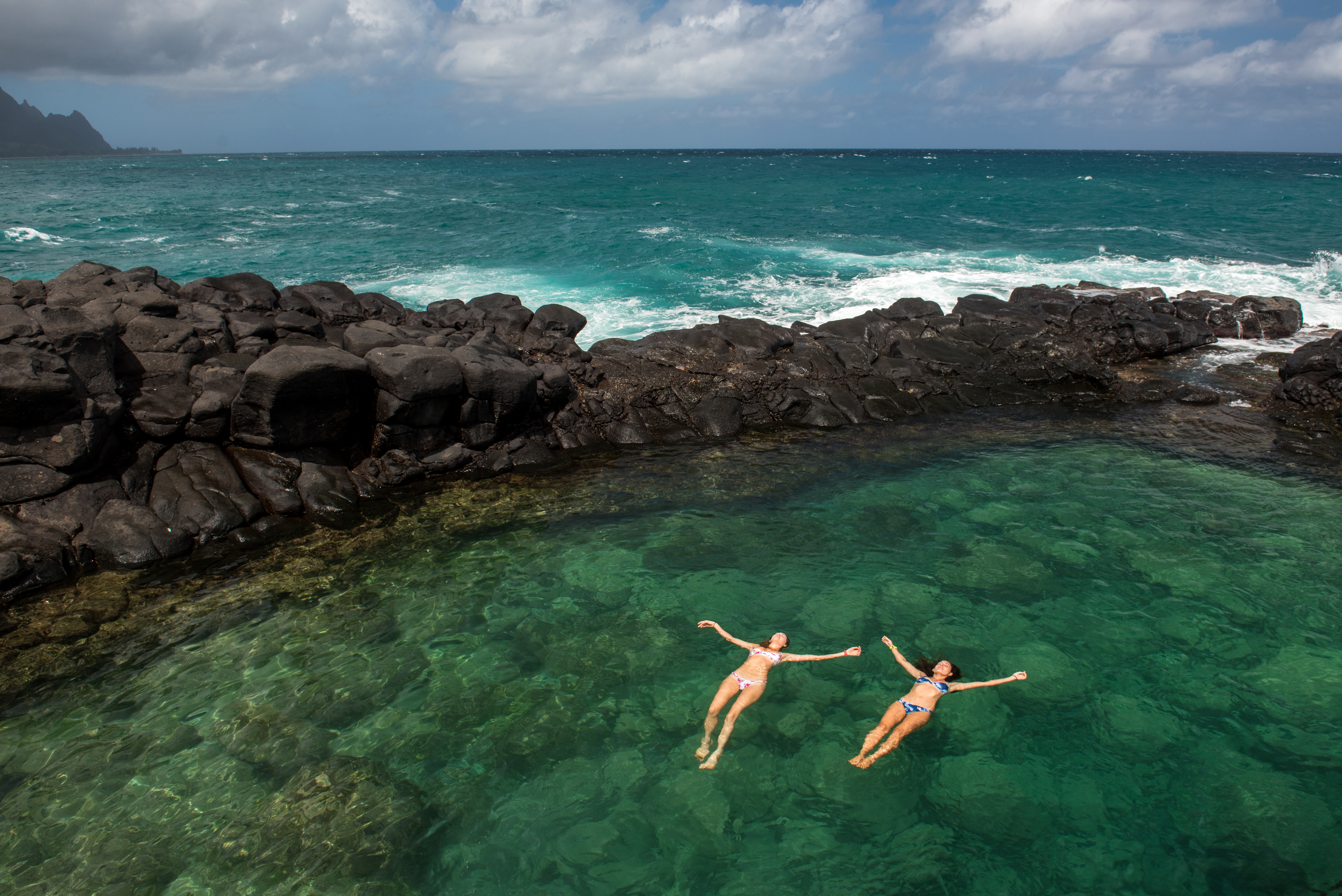 Lexi Grinpas and Chelsea Yamase floating in Queen's Bath in Princeville, Hawaii as seen on Travel Channel's Top Secret Swimming Holes episode TUSH202H.