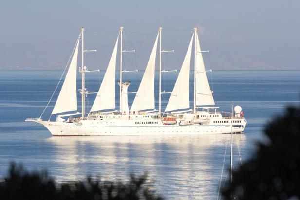 A tall ship or clipper from the Windstar Cruises sails past in Mykonos Town. It is called Wind Star, a 4-masted sailing yacht.