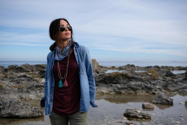 Hero shot of Megan posing, ready for her next adventure, in the middle of a rock formation stretching out into the sea.