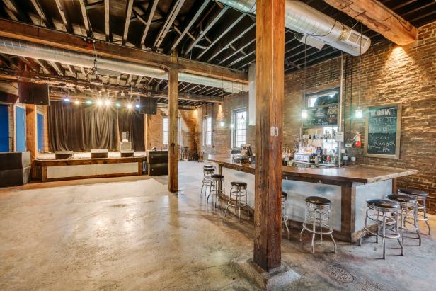 An empty, well-lit open venue space complete with bar and stage 