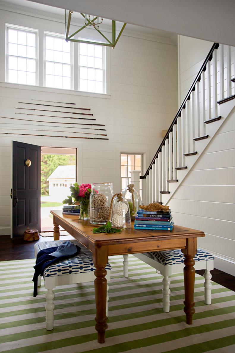 A two-story white foyer features an antique wooden dining table.