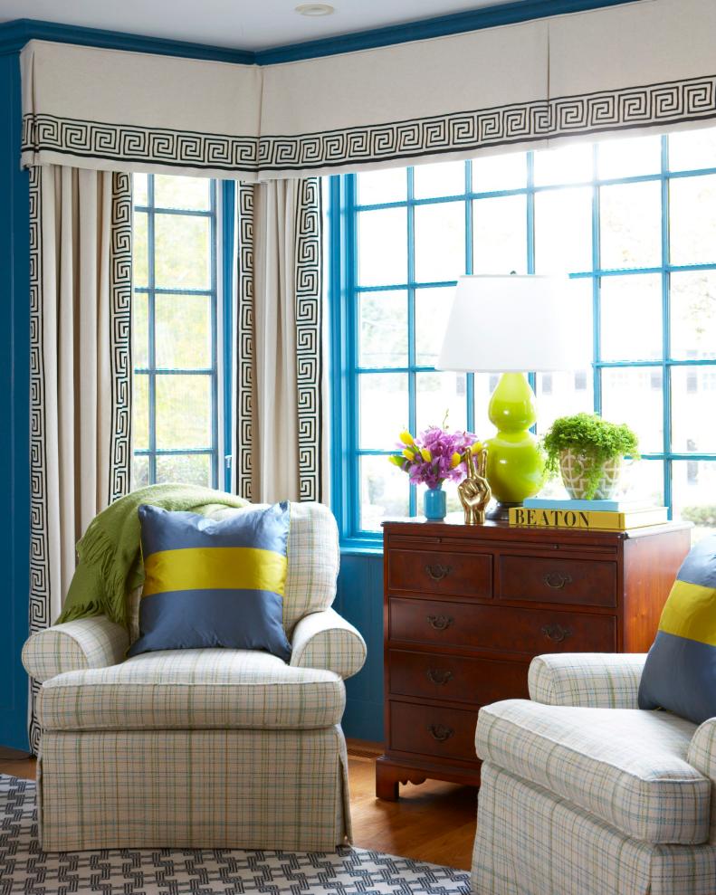 A dresser and two plaid armchairs stand before a teal-painted window.