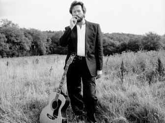 Guitarist Eric Clapton in a field of long grass with his guitar, Surrey, 1993