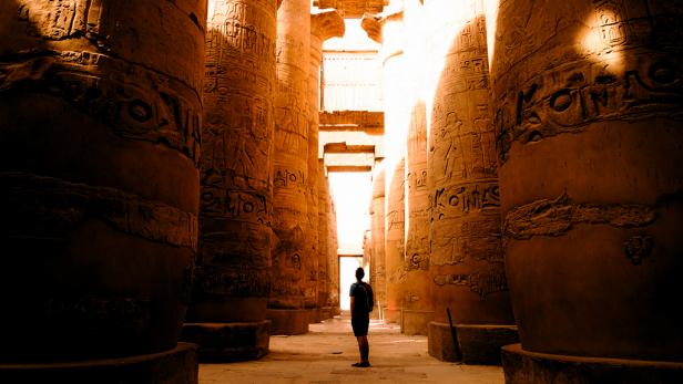 man stands in ancient egyptian ruin with sunlight filtering in