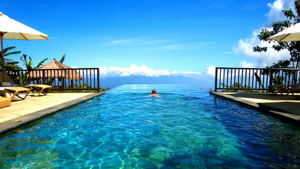 woman lays at the end of an infinity pool during the day blue water