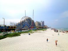 view of beach with people, ocean, and amusement park rides, ferris wheel