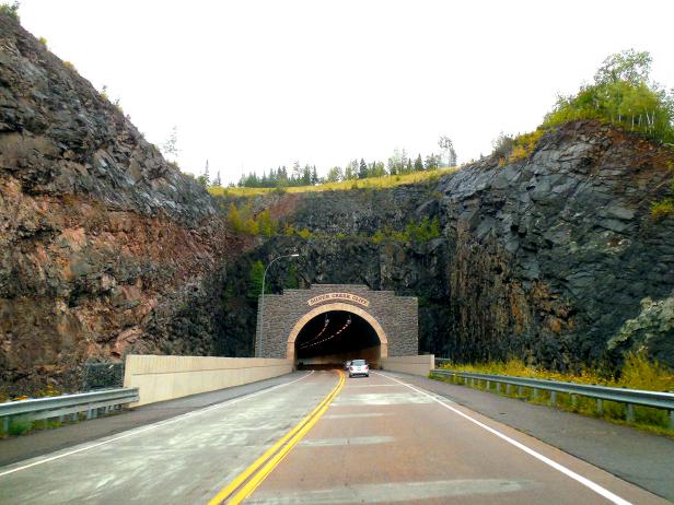 car entering large tunnel with tall cliffs on each side