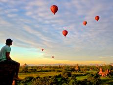 man sitting high on right side of photo watching air balloons over temples in bagan myanmar during a sunset
