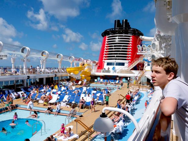 teen leaning over railing on disney line cruise ship with outdoor pool on lower deck