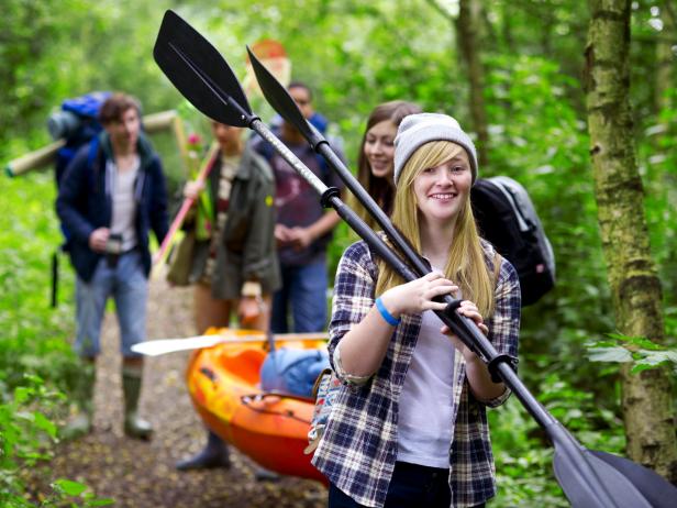 teenagers walking in a line down a trail carrying camping and kayaking gear