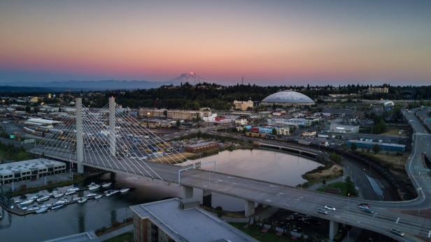 Aerial shot of downtown Tacoma, including the East 21st Street Bridge, the Tacoma Dome and the Thea Foss Waterway. In the distance, Mt Rainier looms against the colorful sunset.