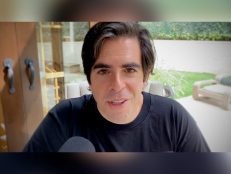 Eli Roth, host of the "A Ghost Ruined My Life" podcast, is seated in front of a microphone, wearing a black t-shirt. There is a patio behind him.
