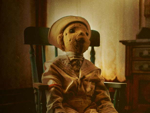 A replica of Robert the Doll is seated in a wooden chair.