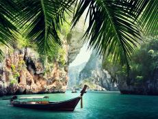 Tropical Water With Single Longtail Boat Surrounded By Massive Rock Structures