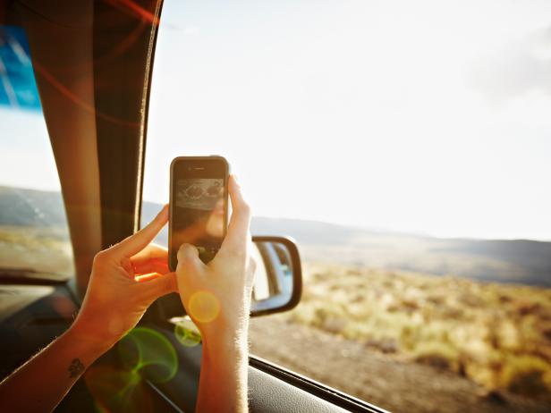 Woman riding in front seat of car driving through desert taking digital photo with smartphone