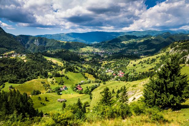 Magnificent sweeping landscape scene in Transylvania, Romania. Rolling green hills and the Carpathian mountains surround picturesque villages in the valley below. Wide angle horizontal image.