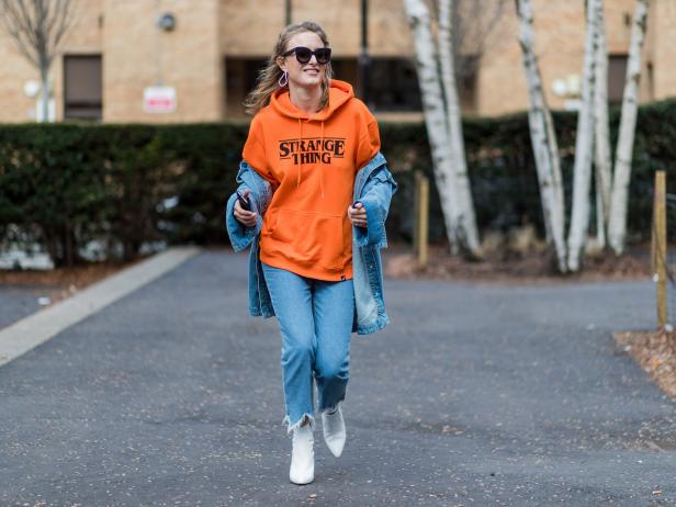 LONDON, ENGLAND - FEBRUARY 19: A guest wearing an orange hoody with the print stange thing, denim jacket, and denim jeans outside Topshop Unique on day 3 of the London Fashion Week February 2017 collections on February 19, 2017 in London, England. (Photo by Christian Vierig/Getty Images)