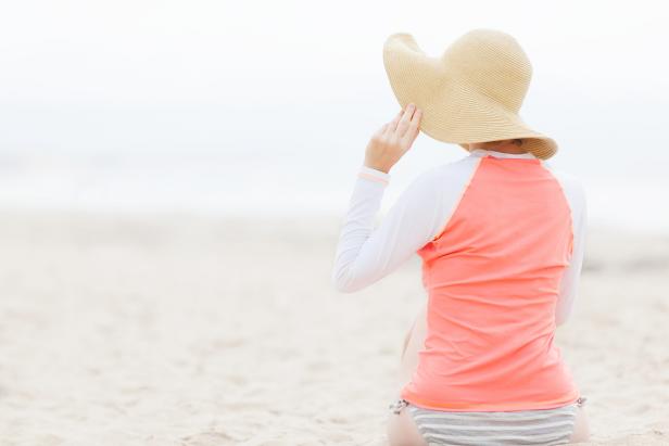 young woman in rashguard at the beach protecting her skin from the sun, uv protection concept
