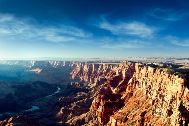 Arizona's Grand Canyon glows red and yellow, a vibrant blue sky and clouds still visible above as the sun sets.  Horizontal with copy space.