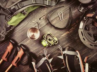 Climber accessories set on dark wooden background:  boots with crampon, backpack, sunglasses, flashlight and others. Top view