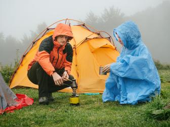 Tourists cooking coffee on primus near the tent in the mountains. Foggy and rainy camping while hiking.