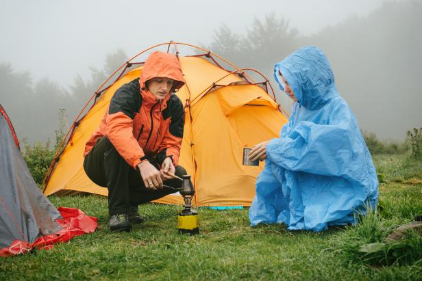 Tourists cooking coffee on primus near the tent in the mountains. Foggy and rainy camping while hiking.