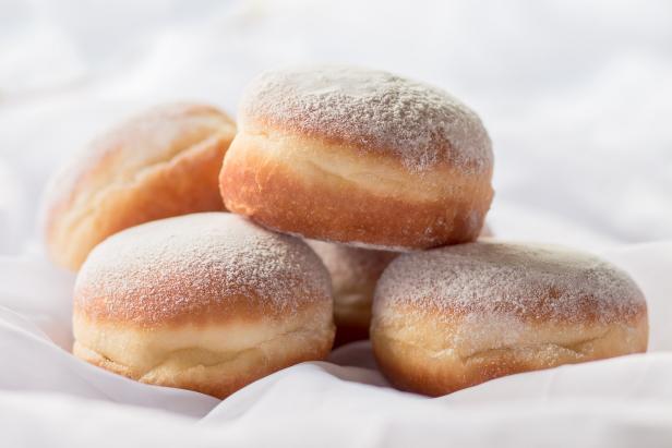 Jelly filled doughnuts with powdered sugar on a bed with white sheets