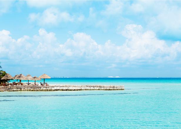 Subject: Horizontal view of the vacation resort hotel on the island of Isla Mujeres, with pristine white sandy beach that face the gentle waves of the aqua blue Caribbean Sea in the glow of morning sunlight. 