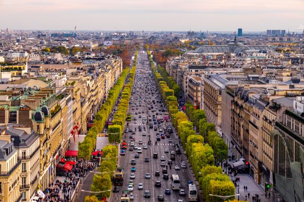 The Avenue des Champs-Ã lysÃ©es in late autumn seen from the Arc de Triomphe. Orange and yellow tree leafs with heavy traffic in the middle. Old buildings on both sides.