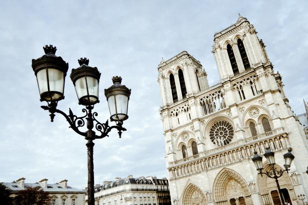 Looking upwards at the Notre Dame Cathedral in Paris, France with a street light in the foreground. 