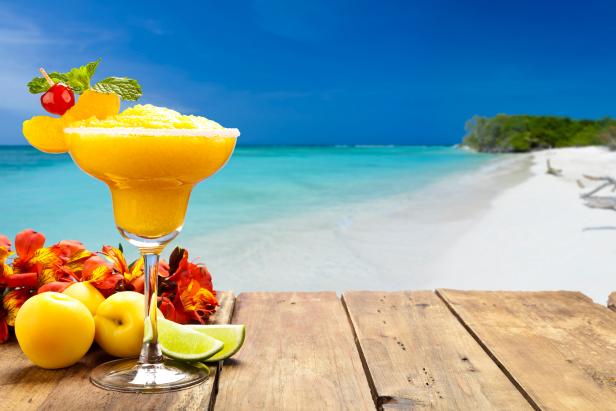 Peach daiquiri on wood table against tropical beach background. The glass is placed at the left of the frame leaving a useful copy space at the center-right
