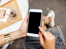Woman holding a smart phone with empty screen sitting outdoors at the cafe with cake and coffee on the table