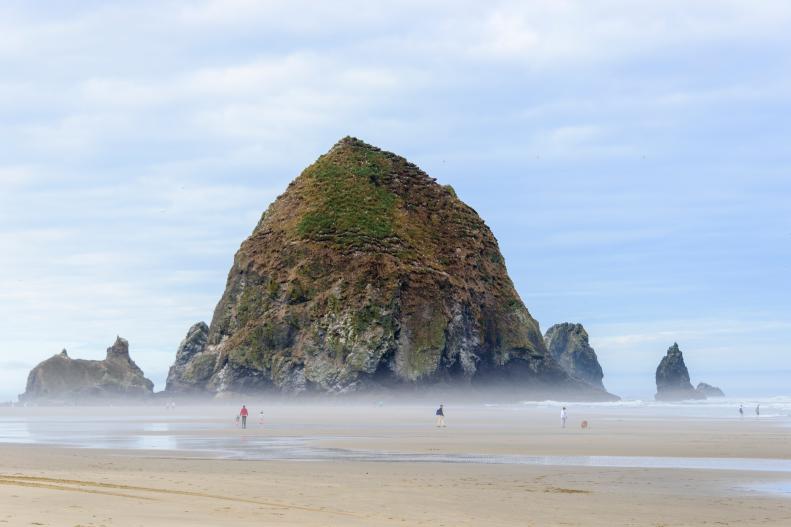 People enjoying a day at Cannon Beach, Oregon. The formation known as Haystack Rock can be seen in the background.