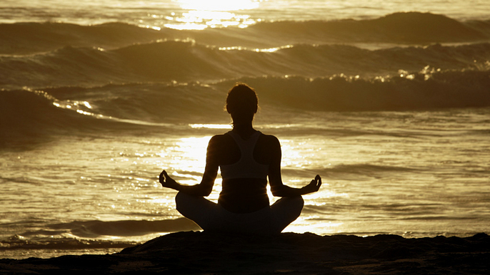 Woman meditating on beach at sunrise